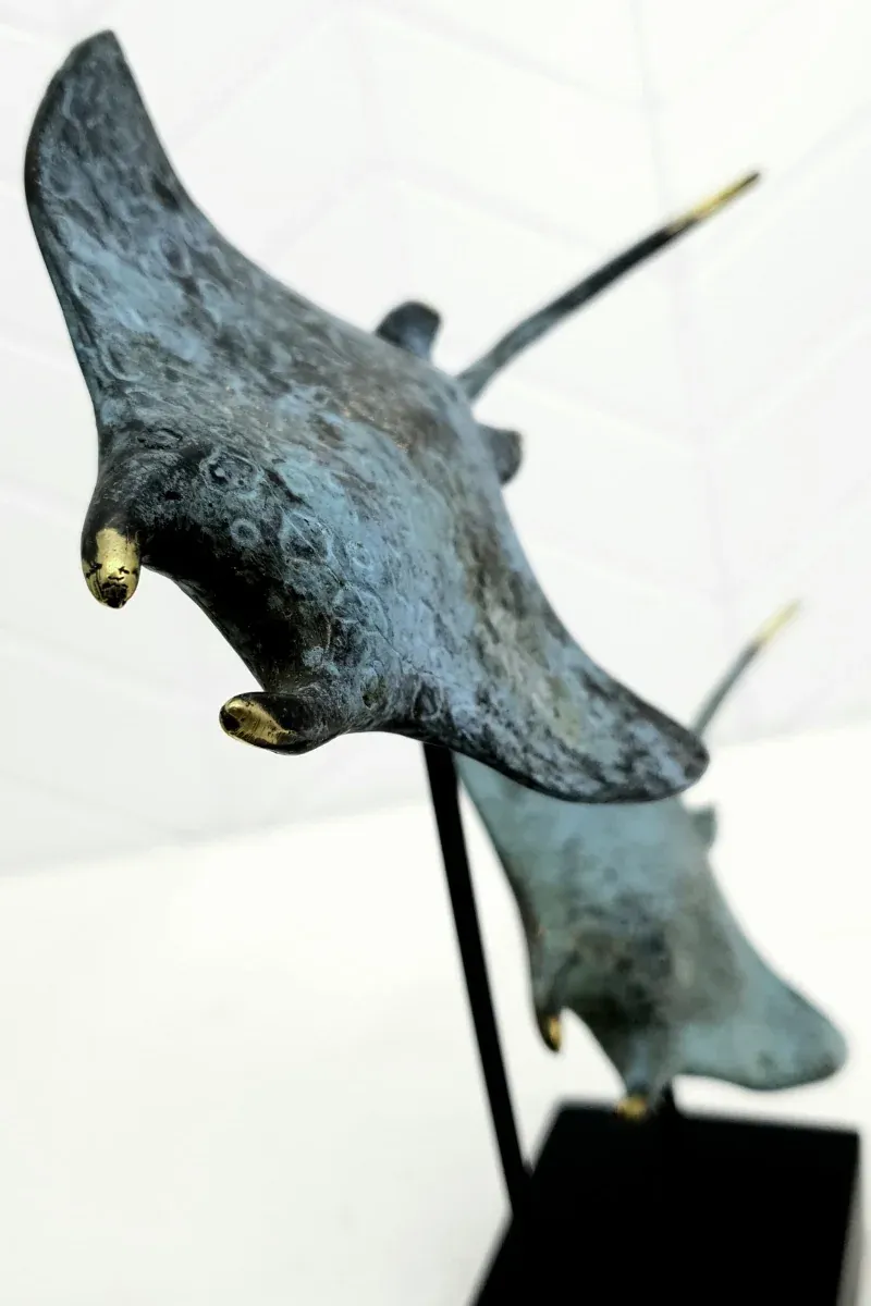 Close-up of the Twin Manta Ray sculpture: blue-green patinated bronze with hand-gilded wing tips